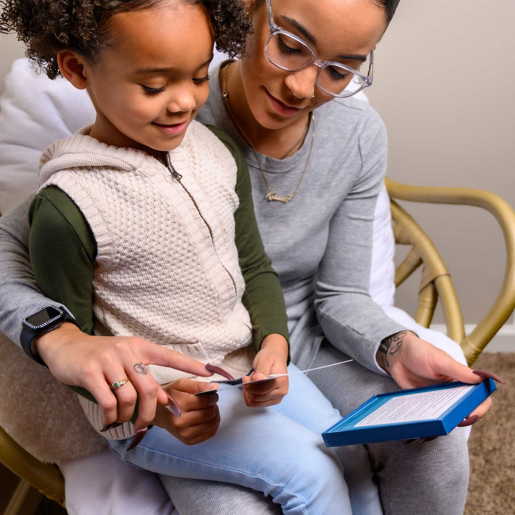 A Black mother and daughter sitting together, excitedly playing the guess who game with the Legendary Leaders - Black History Flash cards that list African American history facts about famous black people for kids.